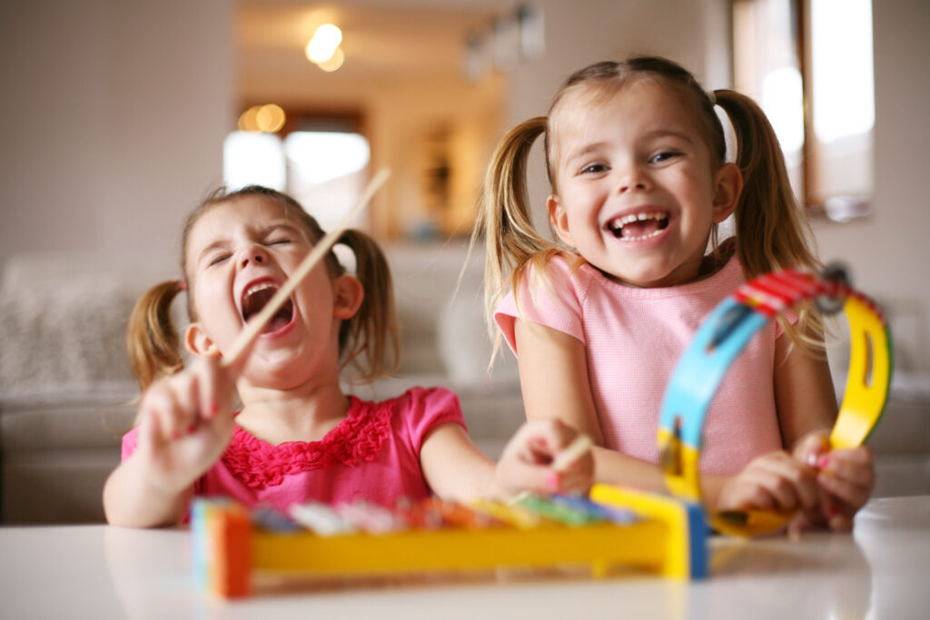 Kinder und Musik: Zwei Mädchen musizieren lachend am Tisch