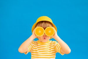 Sommerspaß im Revier: Kind mit Hut auf und Orangenscheiben vor den Augen
