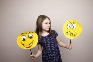 Tipps für den Schul- und Kindergartenstart: Mädchen mit lachendem und wütendem Emoji in der Hand