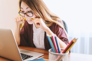 Weiterführendes Studium: Junge Frau mit Brille sitzt vor Laptop mit Stift im Mund