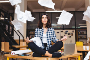 Ausbildung: Junger Mensch sitzt im Schneidersitz auf Schreibtisch und wirft Papier in die Luft