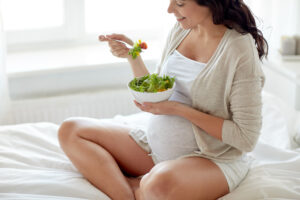 Vegan ernähren in Schwangerschaft und Stillzeit: Schwangere essend im Schneidersitz