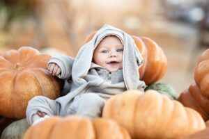Babys erster Herbst: Baby im grauen Anzug mit Ohren zwischen Kürbissen