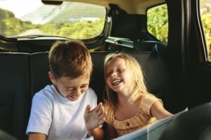 Reisen mit Kindern: Zwei Kinder lachend auf der Rückbank eines Autos