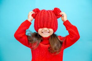Winterhighlights für Familien: Lachendes Kind mit roter Strickmützen über den Augen